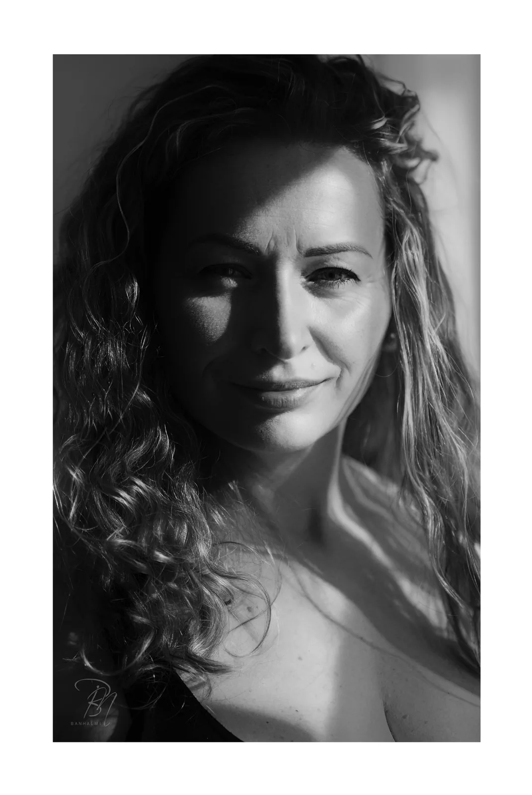Curls in side light — Photo: Norbert Banhalmi Black and white portrait of a woman with curly hair, half her face in shadow.