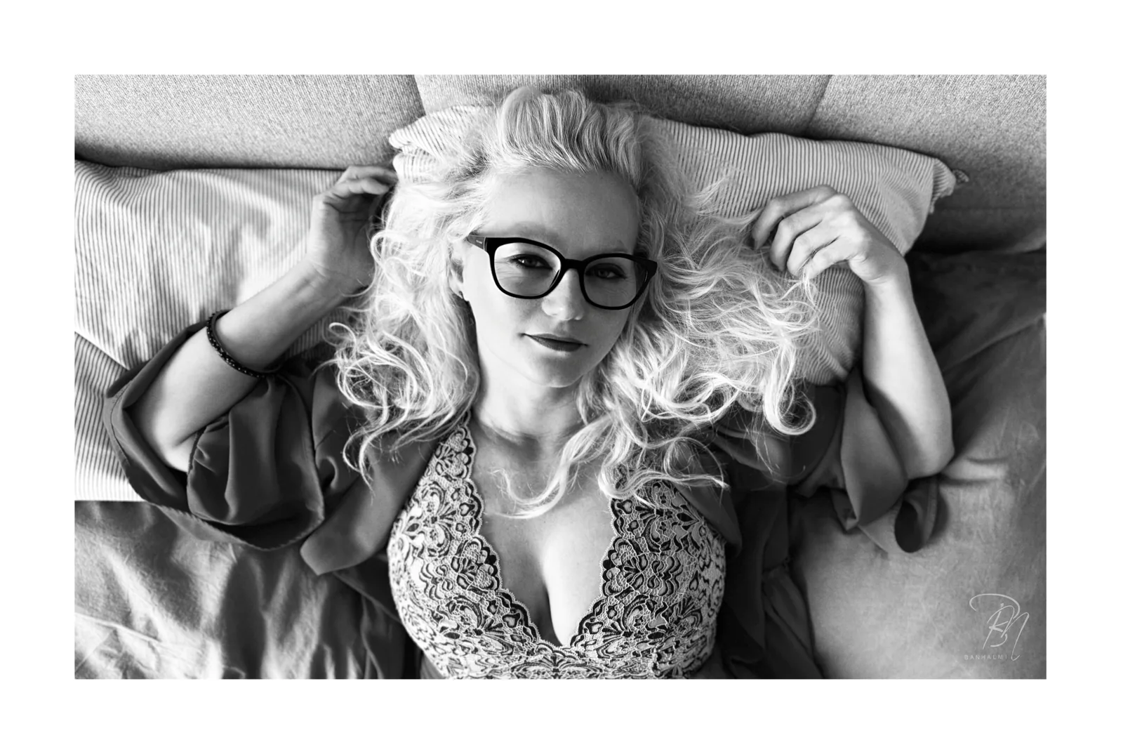 Lying in the light — Photo: Norbert Banhalmi A woman with pale curls and dark glasses lies on a bed, arms above her head.