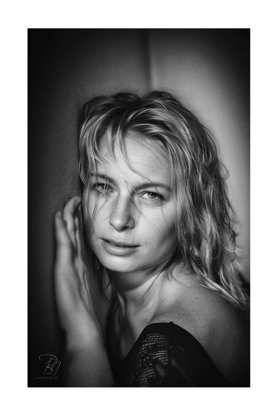 Wall and shoulder — Photo: Norbert Banhalmi A woman leans against a plain wall, hand raised to her hair, shoulder bare.
