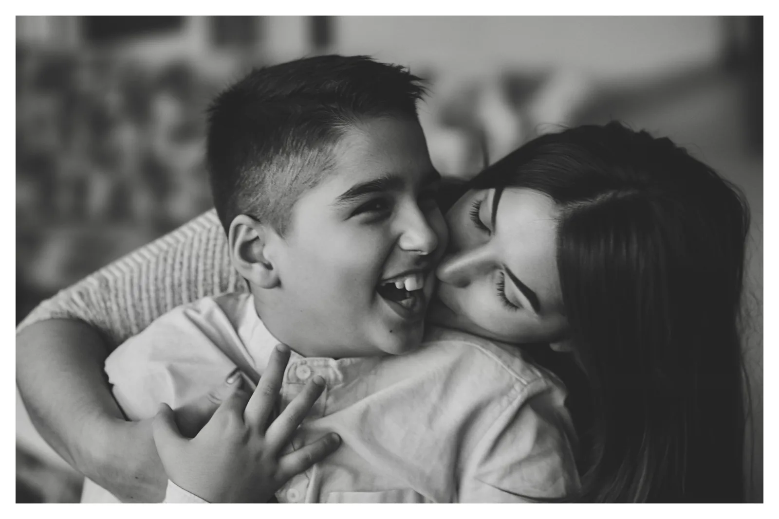 Laughter — Photo: Norbert Banhalmi A boy laughs out loud while a woman kisses his cheek.