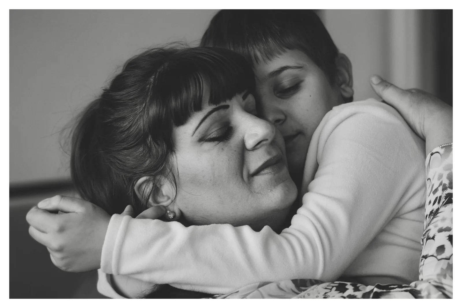 Head on the shoulder — Photo: Norbert Banhalmi A girl rests her head on a woman's shoulder, eyes closed, arms around her.
