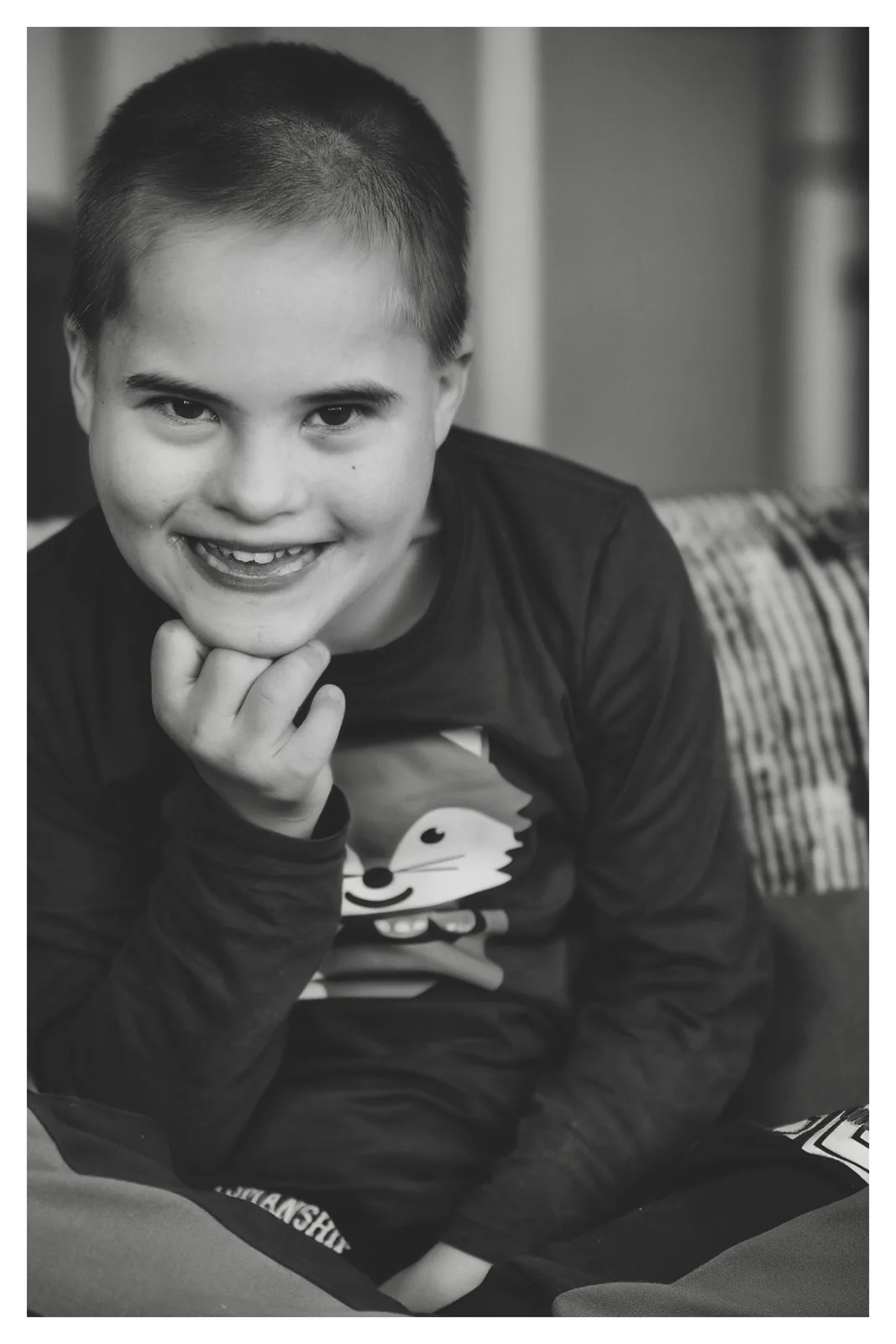 On the sofa — Photo: Norbert Banhalmi A smiling boy sits on a sofa, one hand at his chin.