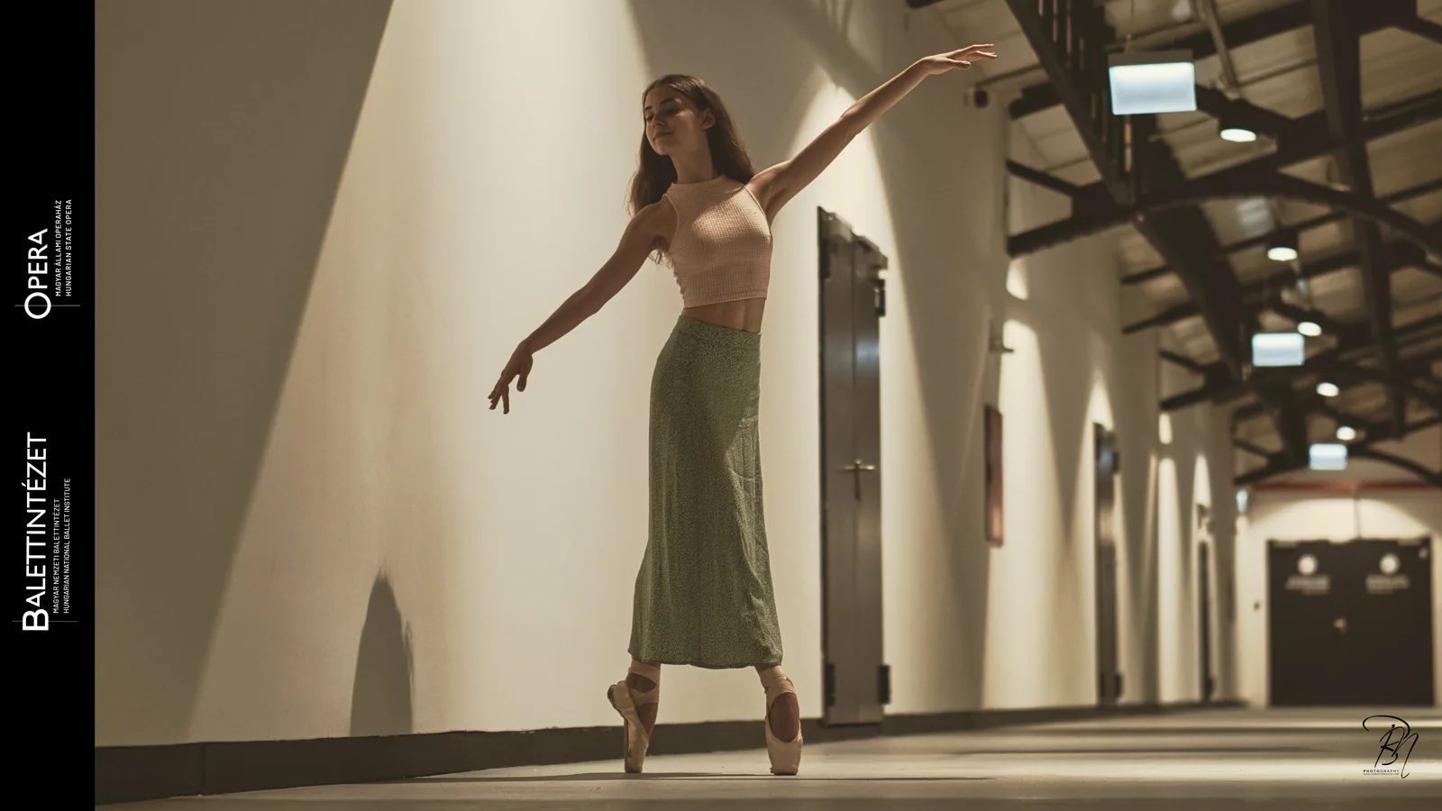 Corridor — Photo: Norbert Banhalmi A dancer turns on pointe in a long empty corridor, arms open.