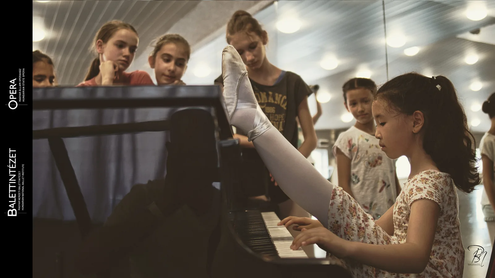 At the piano — Photo: Norbert Banhalmi Children gather around a piano while a teacher's hands rest on the keys.