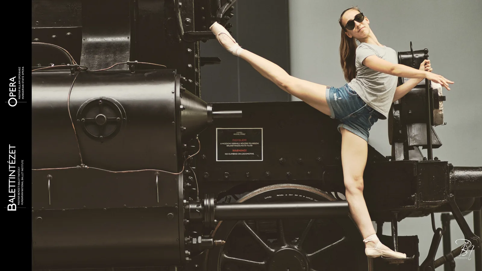 Beside the machine — Photo: Norbert Banhalmi A dancer in denim shorts extends a leg beside an old industrial machine.