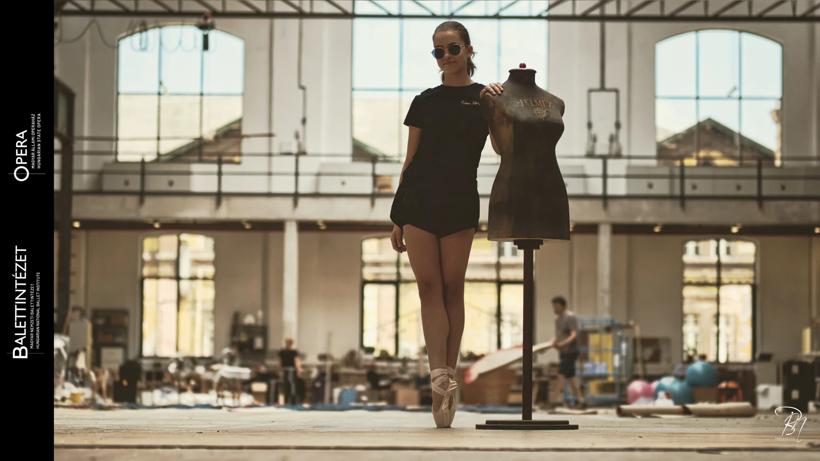 In the hall — Photo: Norbert Banhalmi A dancer stands on pointe beside a dressmaker's dummy in a tall industrial hall.