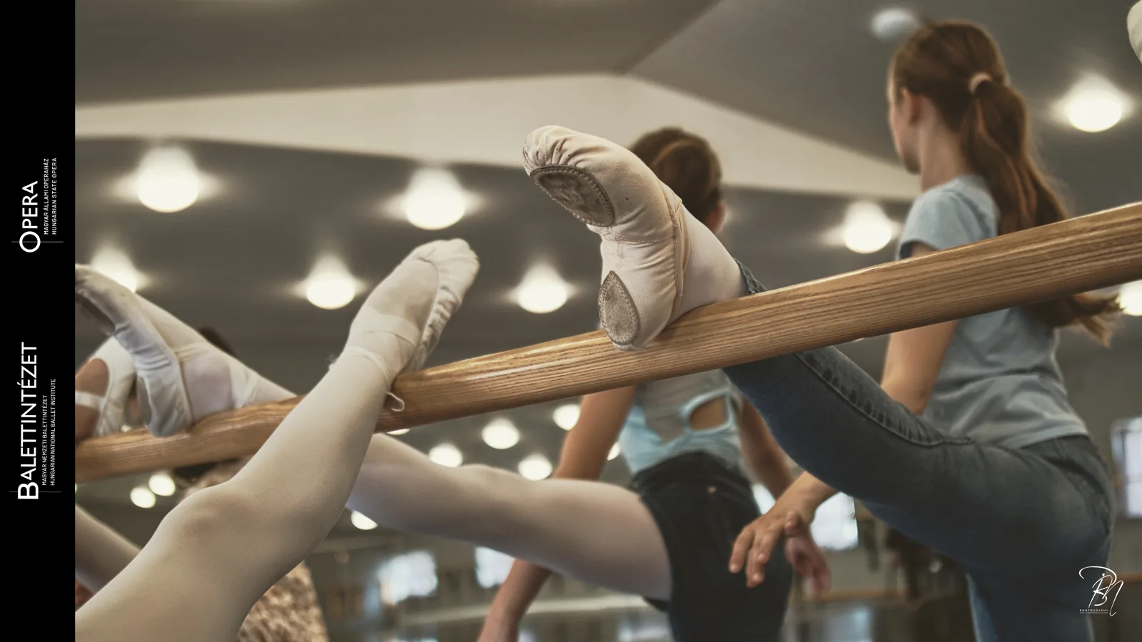 Over the barre — Photo: Norbert Banhalmi A leg stretched over the barre in the foreground, students talking behind.