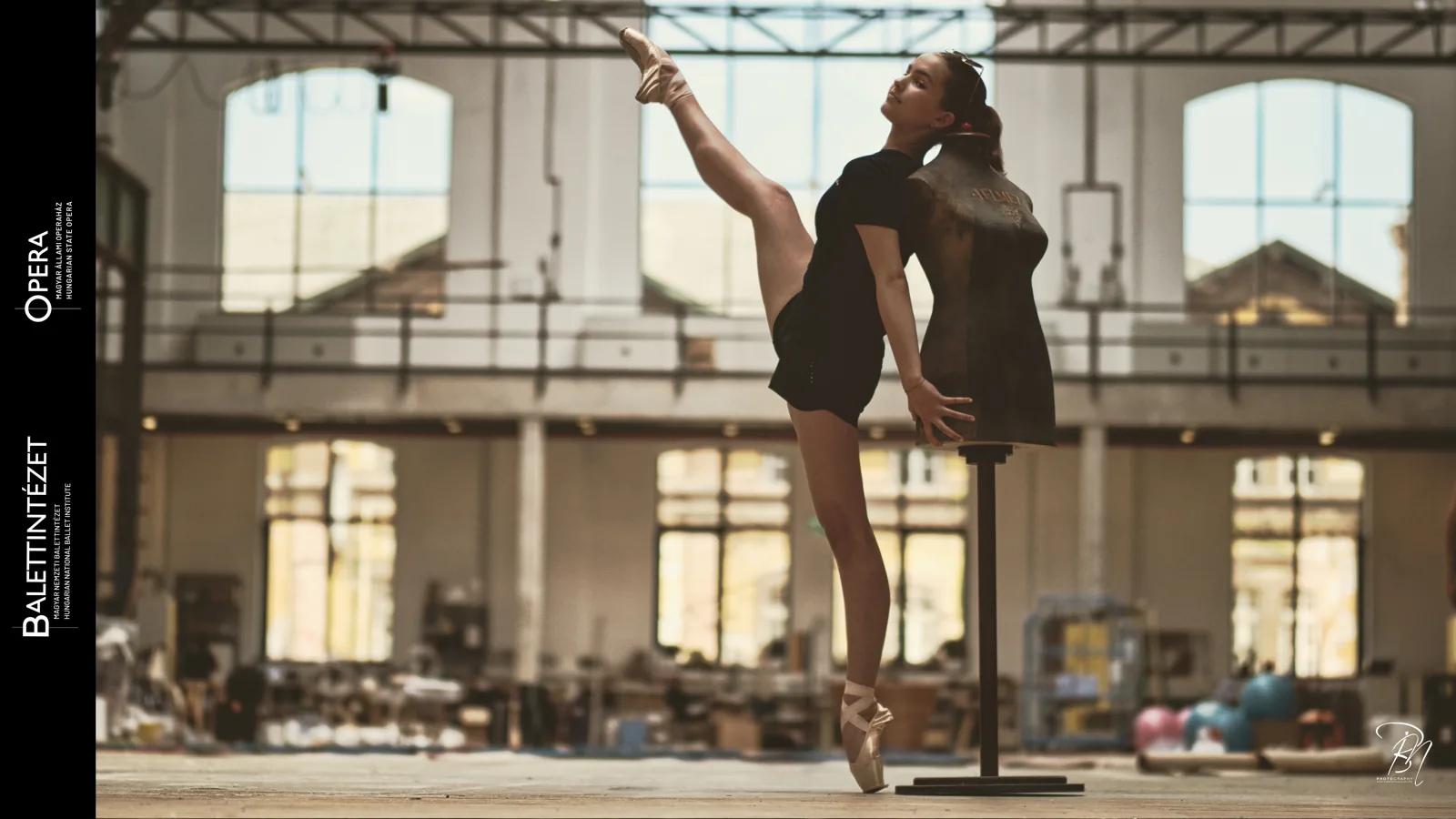 Against the windows — Photo: Norbert Banhalmi A dancer holds a high extension against the tall windows of a workshop hall.