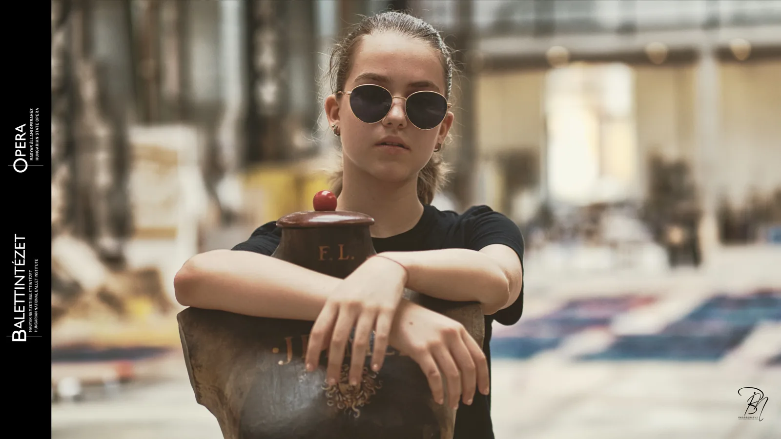 Portrait with sunglasses — Photo: Norbert Banhalmi A young dancer in round sunglasses rests her arms on a rusted object and looks into the lens.
