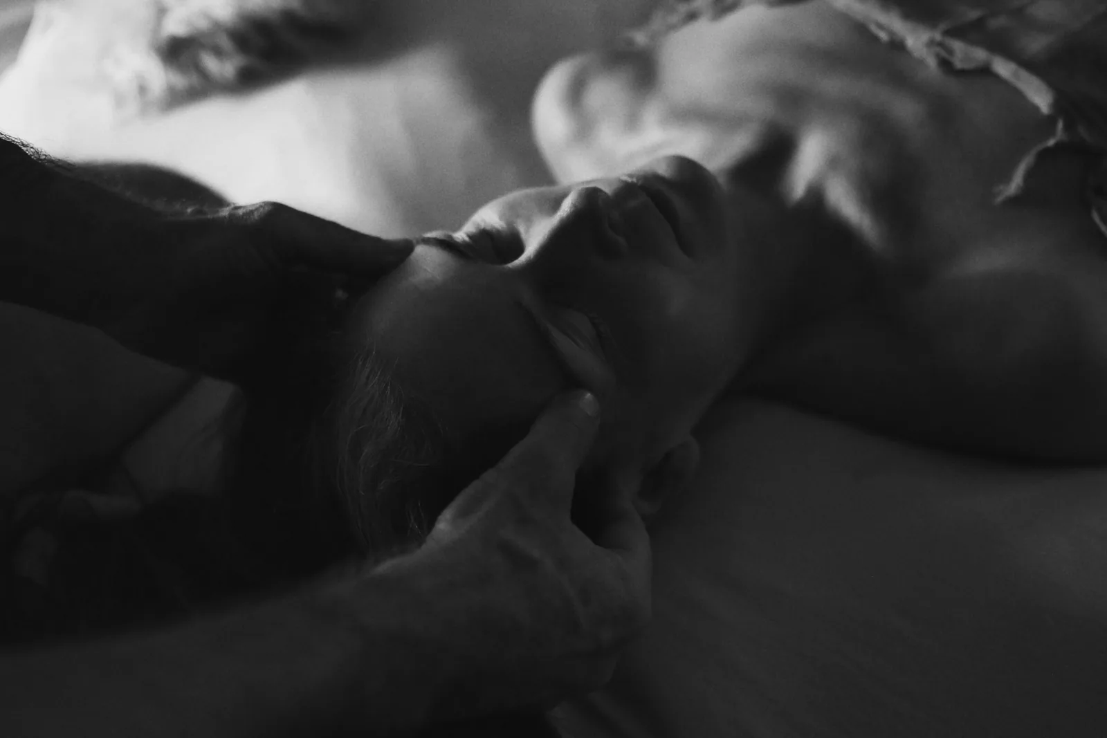 Two bodies in low light — Photo: Norbert Banhalmi Two bodies lie close together in low light, one hand resting on the other's skin.