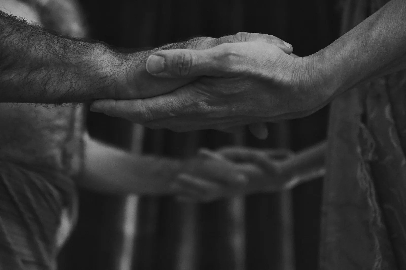 Hands meeting — Photo: Norbert Banhalmi Two hands meet, fingers overlapping, against a dark draped background.