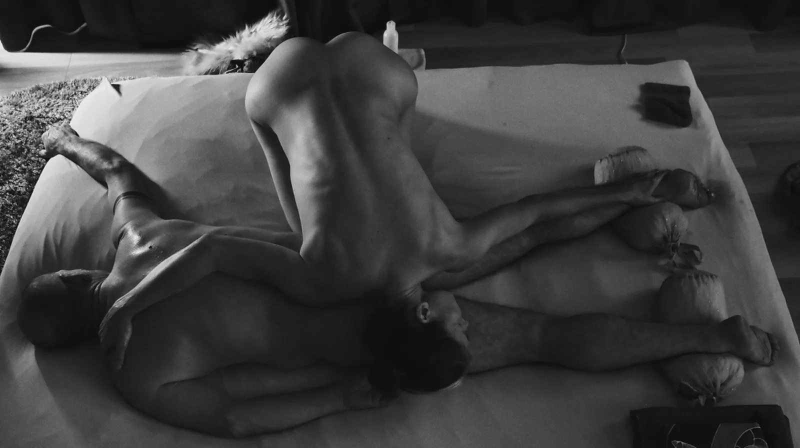 Interlaced — Photo: Norbert Banhalmi Overhead frame of two people on a white sheet, limbs interlaced.
